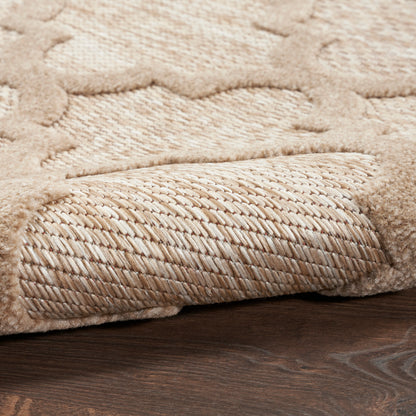 Beige plush area rug with soft pile and raised geometric pattern; rolled edge reveals woven underside on dark wood floor.