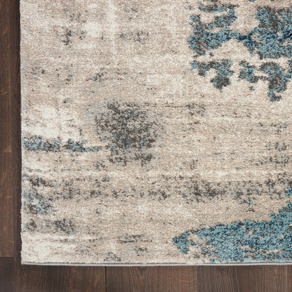 Beige distressed area rug with blue and gray abstract patterns on dark wood floor.