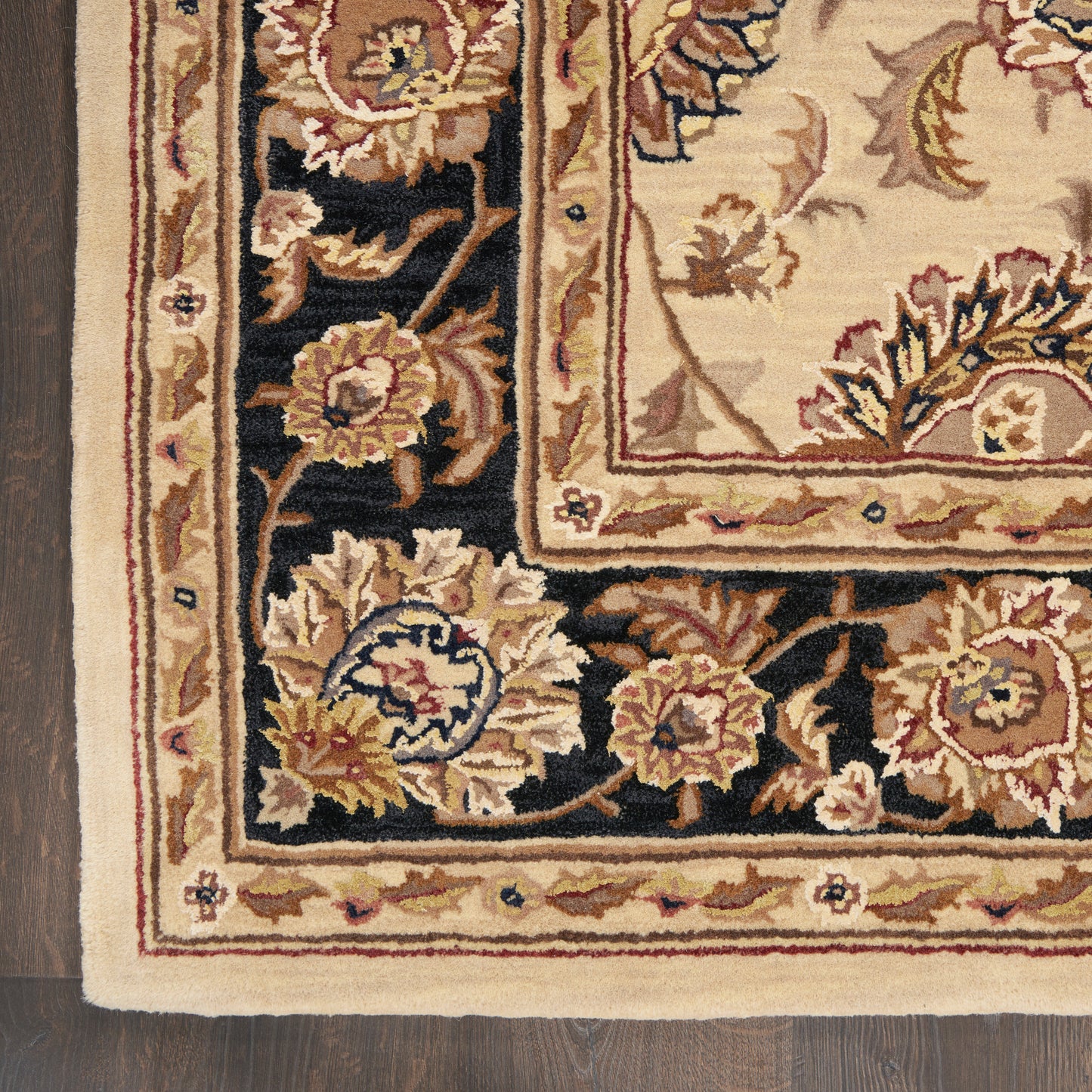 Ornate oriental rug corner with cream and gold floral border on black field; beige fringe edge.