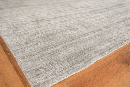 Soft light gray low-pile area rug on warm brown hardwood floor with subtle marled texture