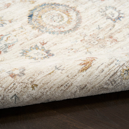 Close-up of a cream rug with faded blue and orange circular medallions, soft textured pile, edge resting on dark wood floor.