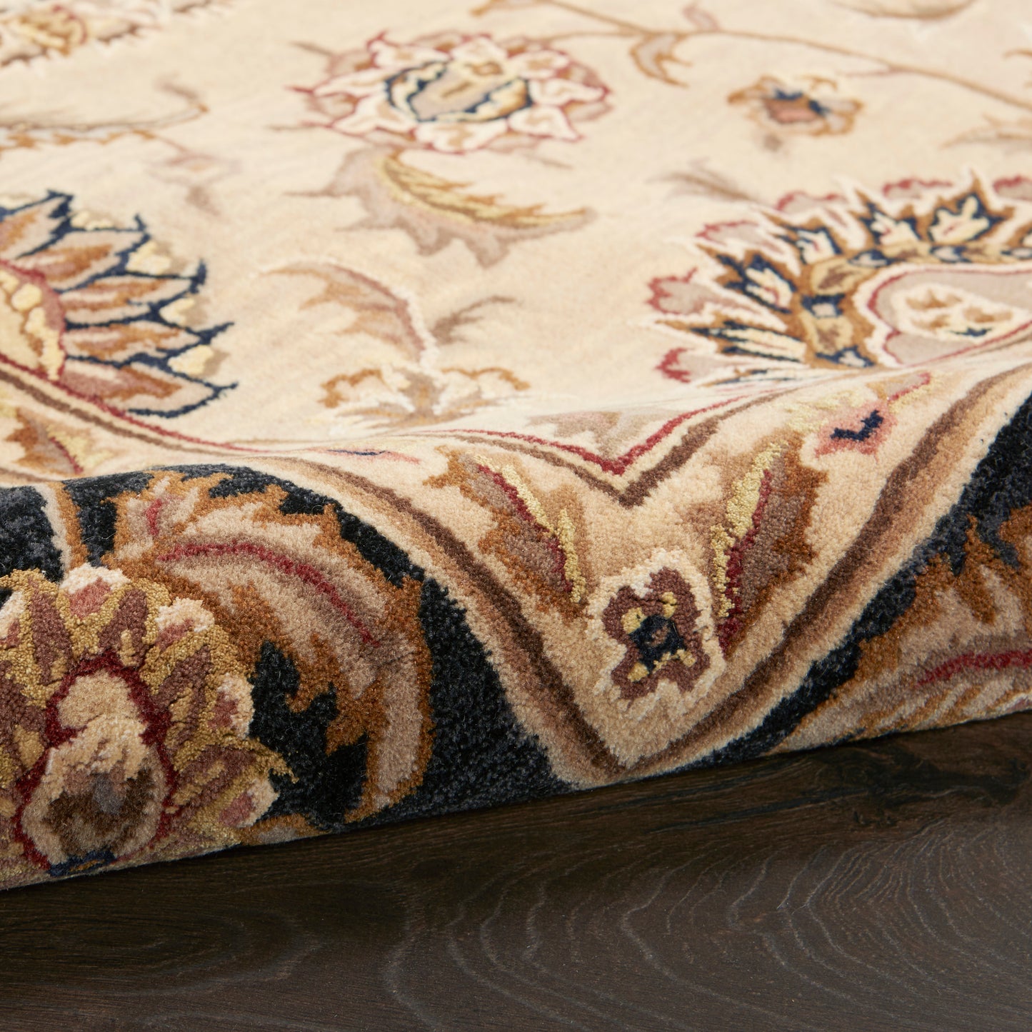 Cream oriental rug with floral motif in gold, blue, and red; plush pile and dark navy border along edge.