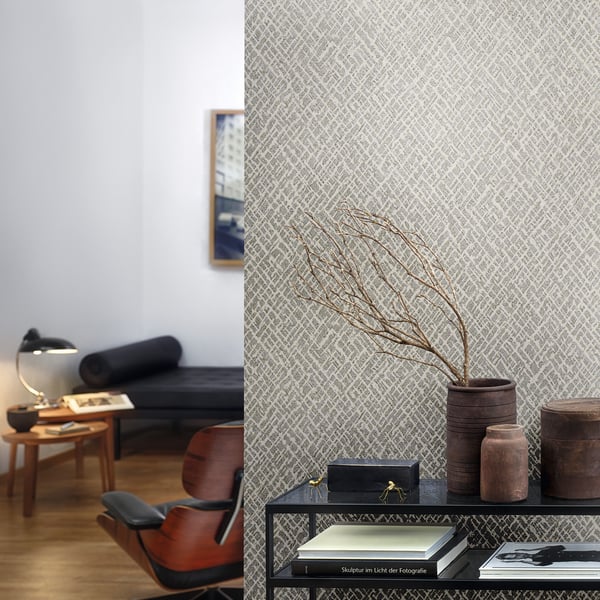 Mid-century living room with leather lounge chair, wooden table, lamp, and ceramic vases on a metal console against patterned wallpaper.
