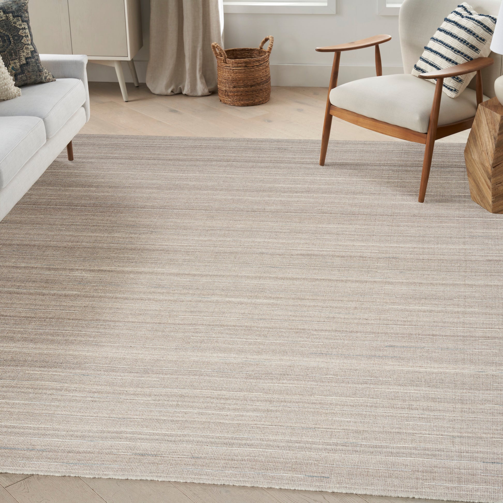 Neutral striped woven rug in beige and gray tones, 5' x 7', in a modern living room with mid-century chairs and a wicker basket.