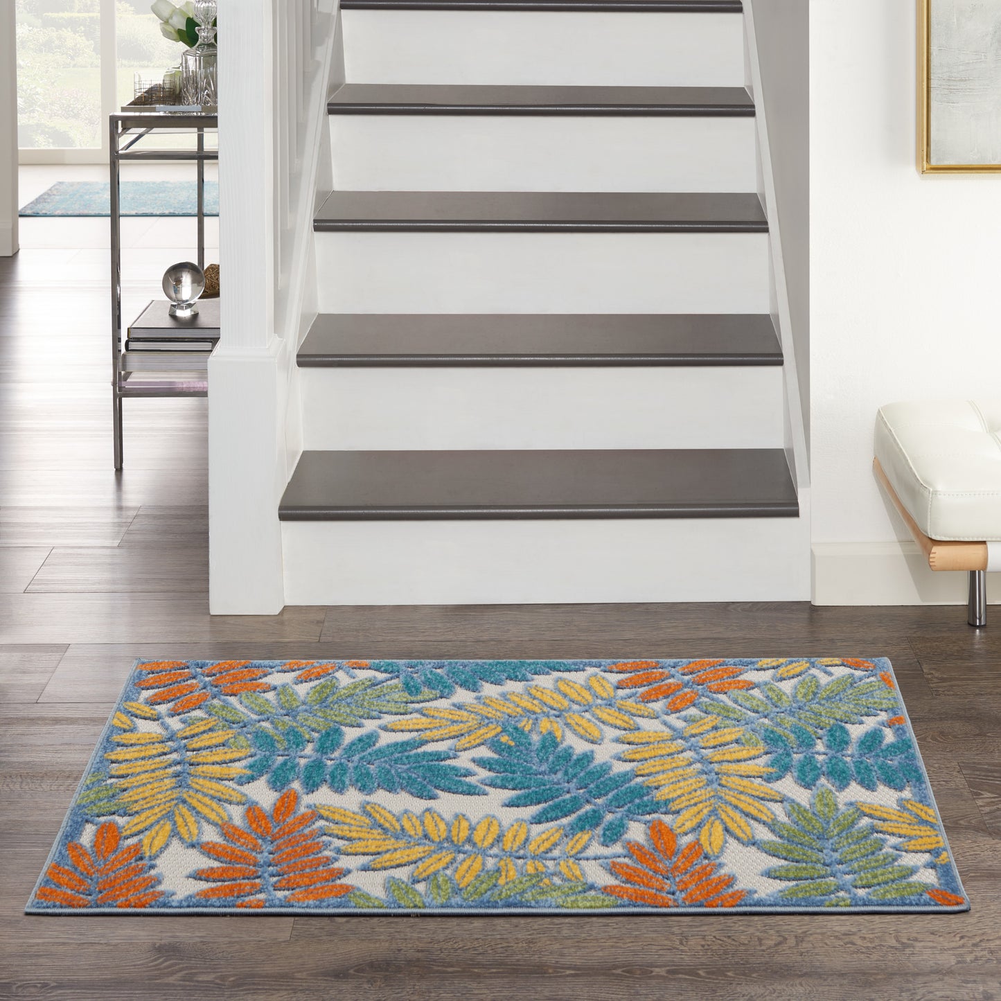 Rectangular rug with teal, orange and yellow palm leaf pattern on a light background at the foot of a white staircase.