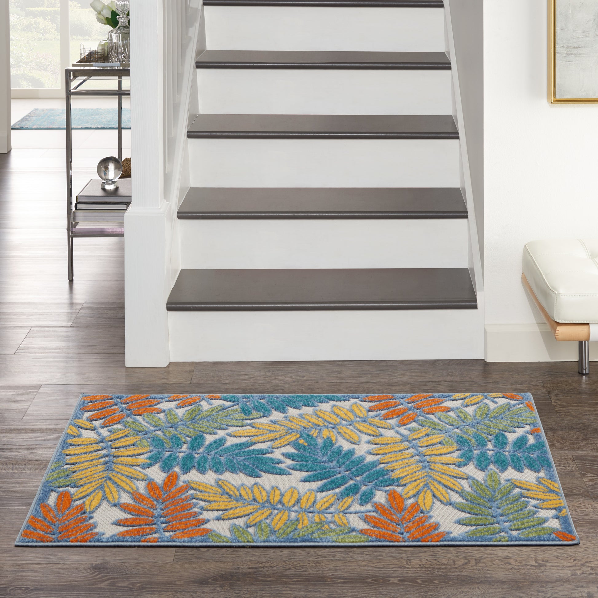 Rectangular rug with teal, orange and yellow palm leaf pattern on a light background at the foot of a white staircase.
