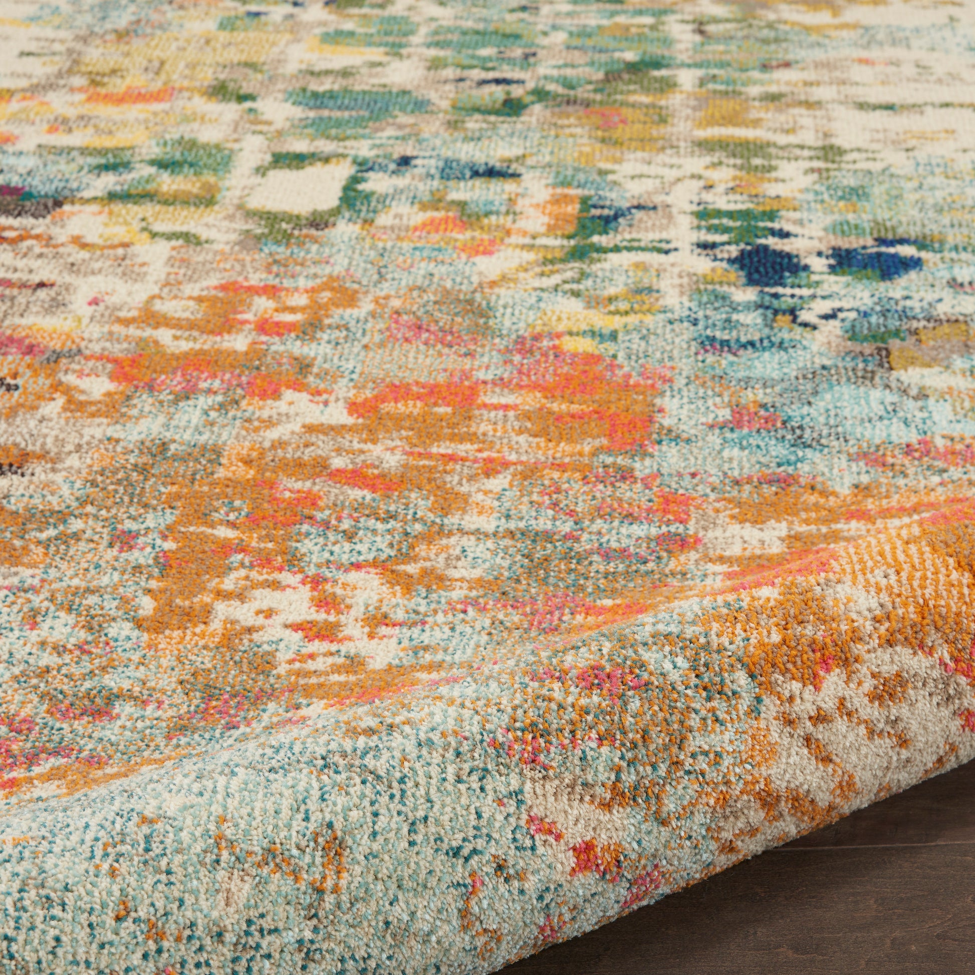 Colorful abstract patterned area rug with teal, orange, pink, and yellow hues; textured pile and folded edge on wood floor