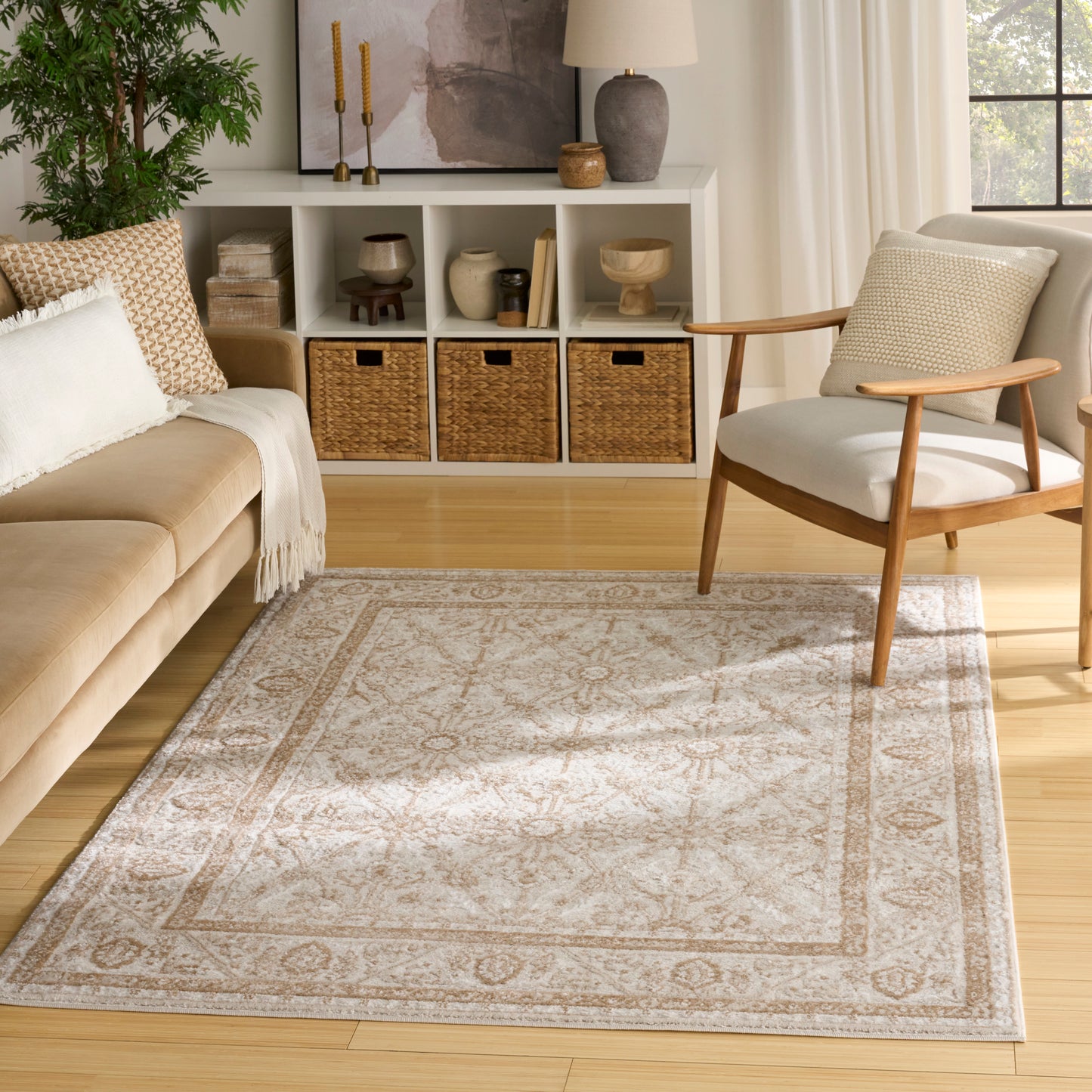 Beige and ivory patterned area rug in a light wood living room with a mid-century chair, beige sofa and wicker baskets.