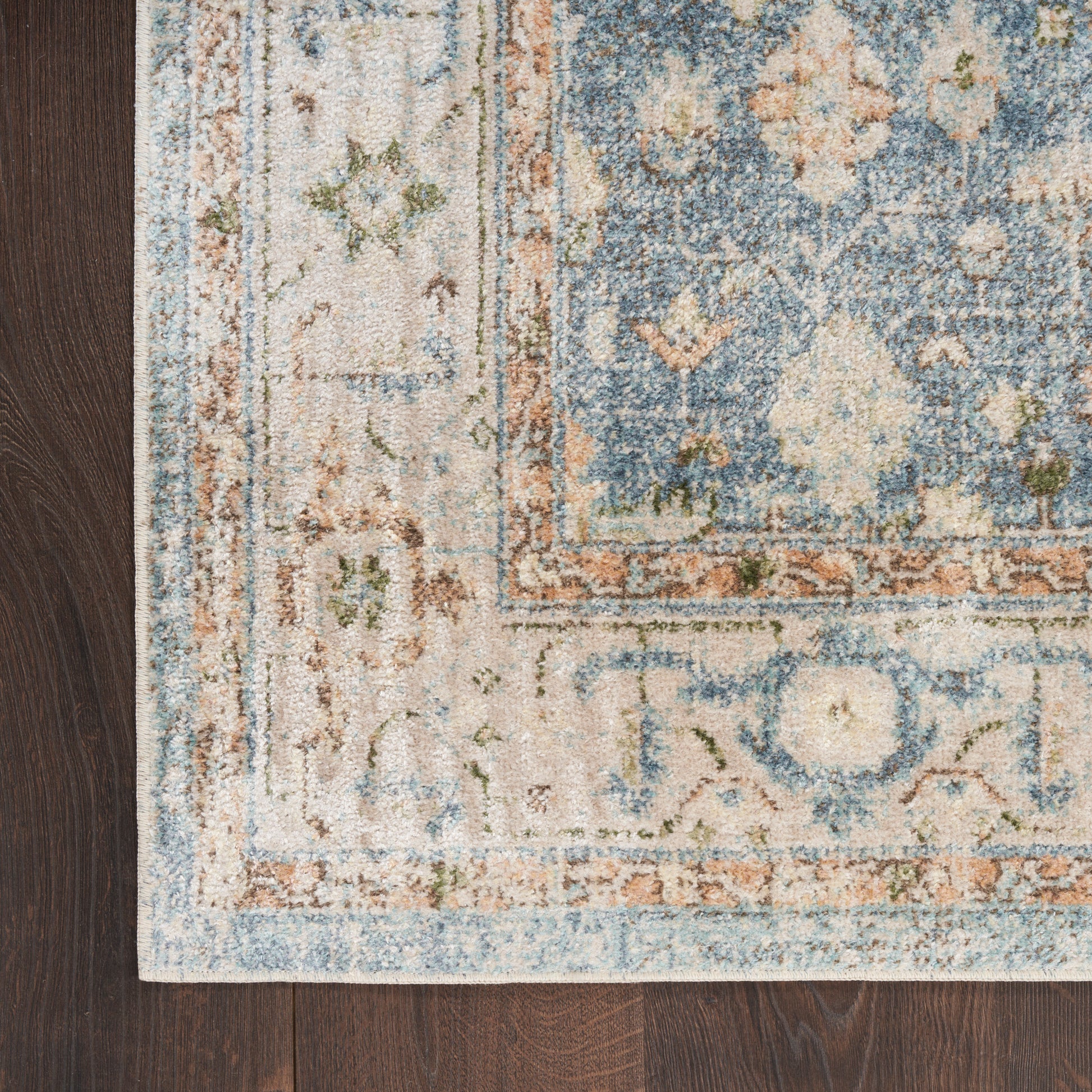 Rectangular Persian-inspired rug with ornate blue, ivory and rust tones on dark wood floor.