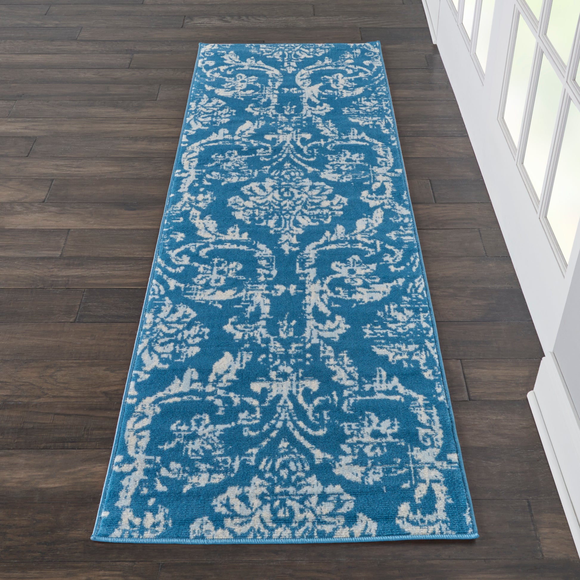 Blue runner rug with white damask pattern on dark wood hallway floor.