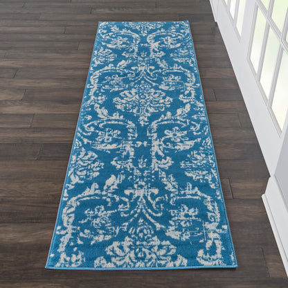 Blue runner rug with white damask pattern on dark wood hallway floor.