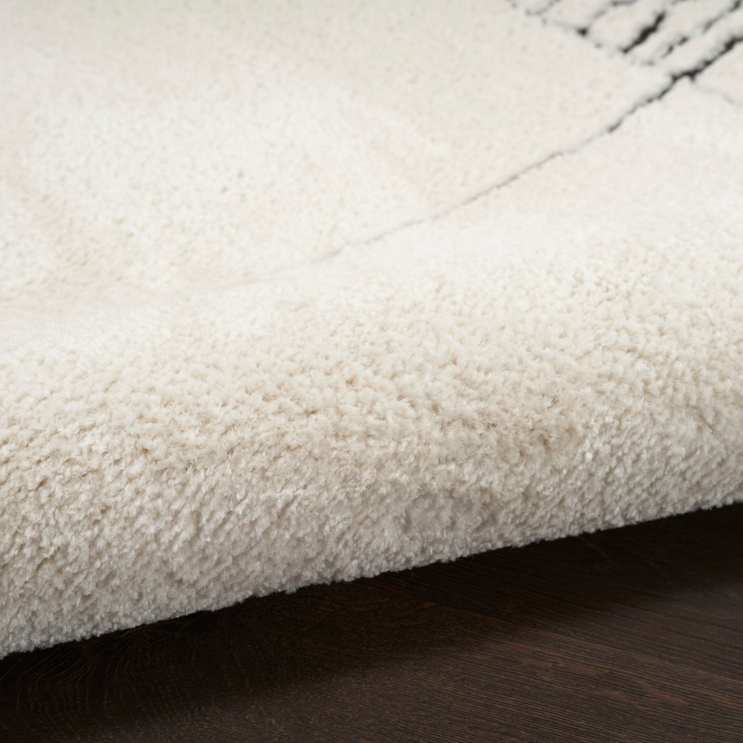 Cream shag rug with thick plush pile on dark wood floor; cozy entryway or bathroom mat.