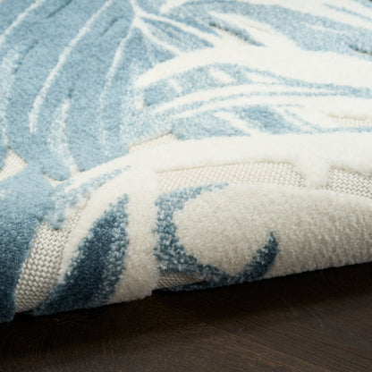 Blue & white plush shag rug with abstract pattern, rolled edge showing underside, on dark wood floor.