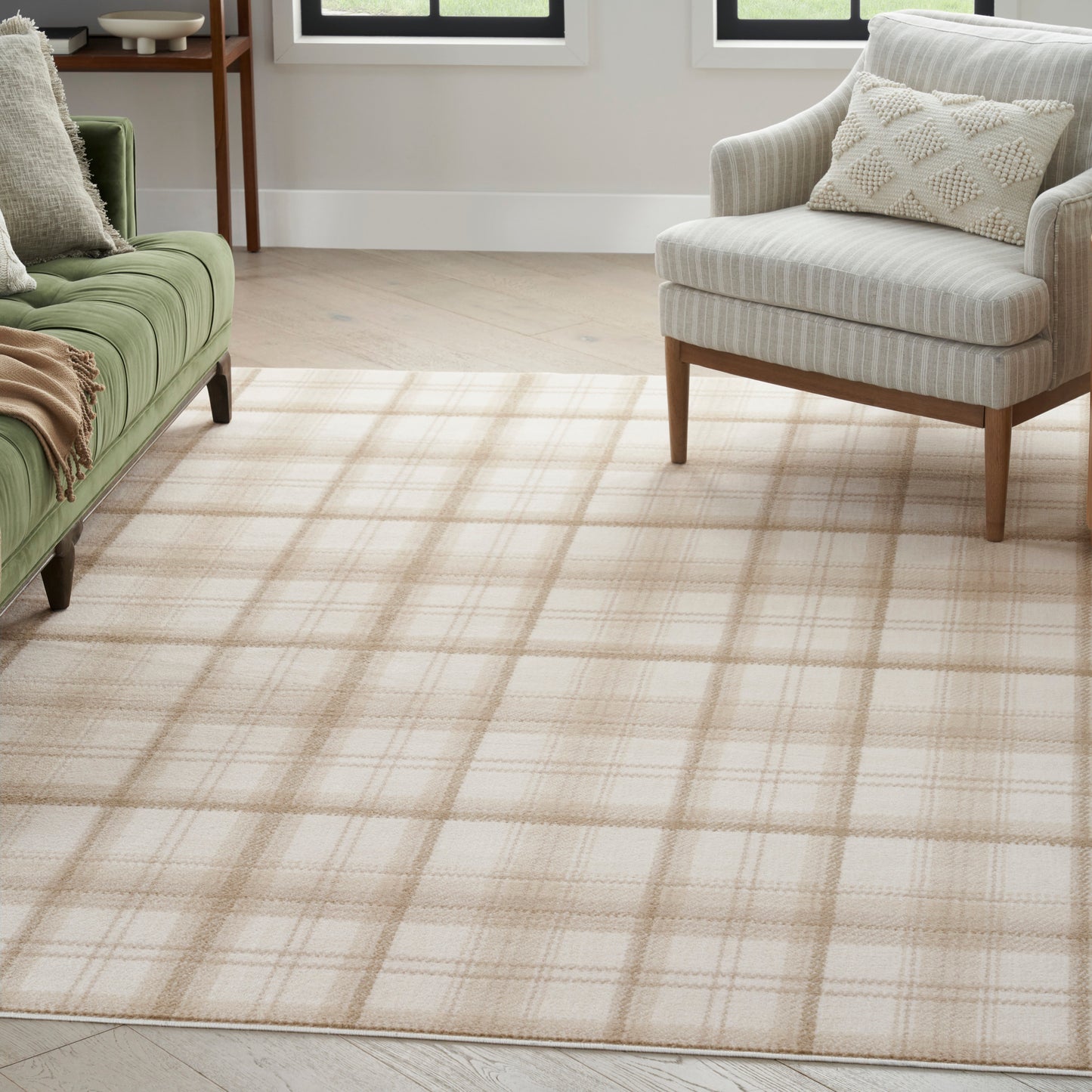 Beige plaid area rug on light wood floor, with green sofa and beige striped armchair in a bright living room.
