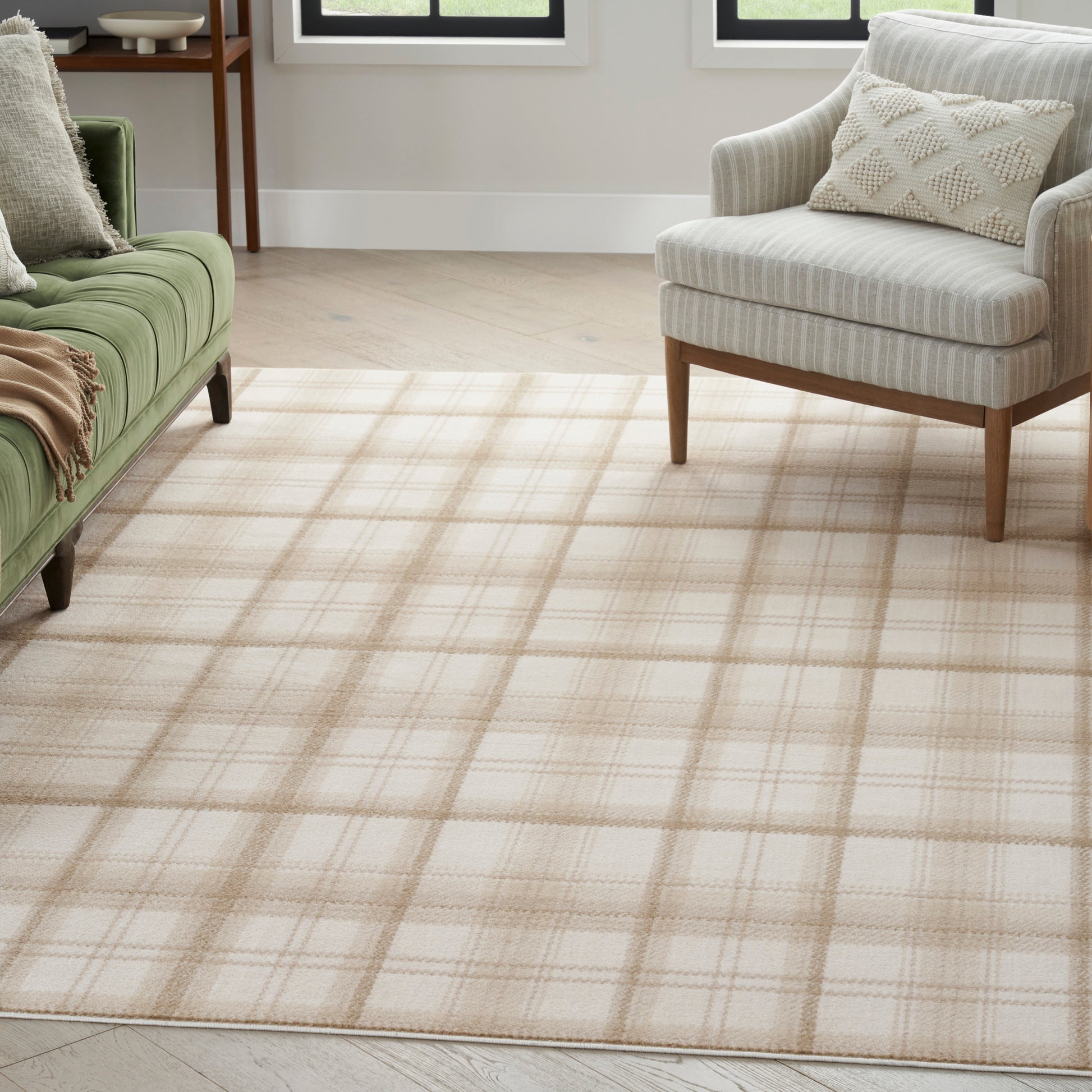 Beige plaid area rug on light wood floor, with green sofa and beige striped armchair in a bright living room.