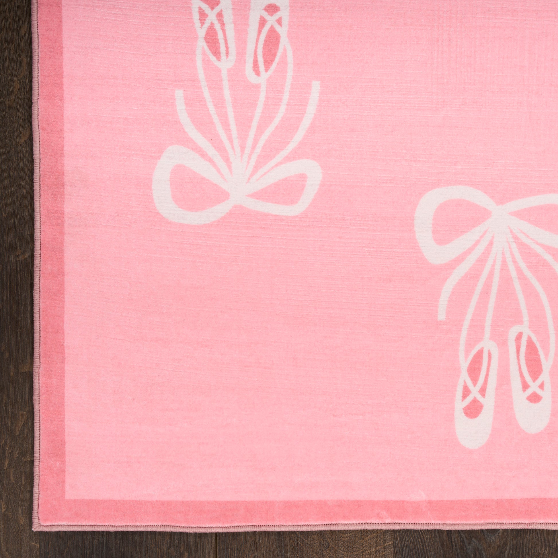 Pink rectangular kids' rug, 5' x 7', featuring white ballet shoe and bow motifs on soft fabric placed on a wood floor.