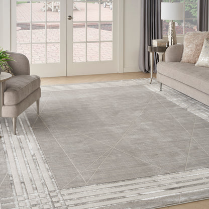 Light gray geometric area rug with white striped border in a contemporary living room with taupe sofa and matching ottoman.