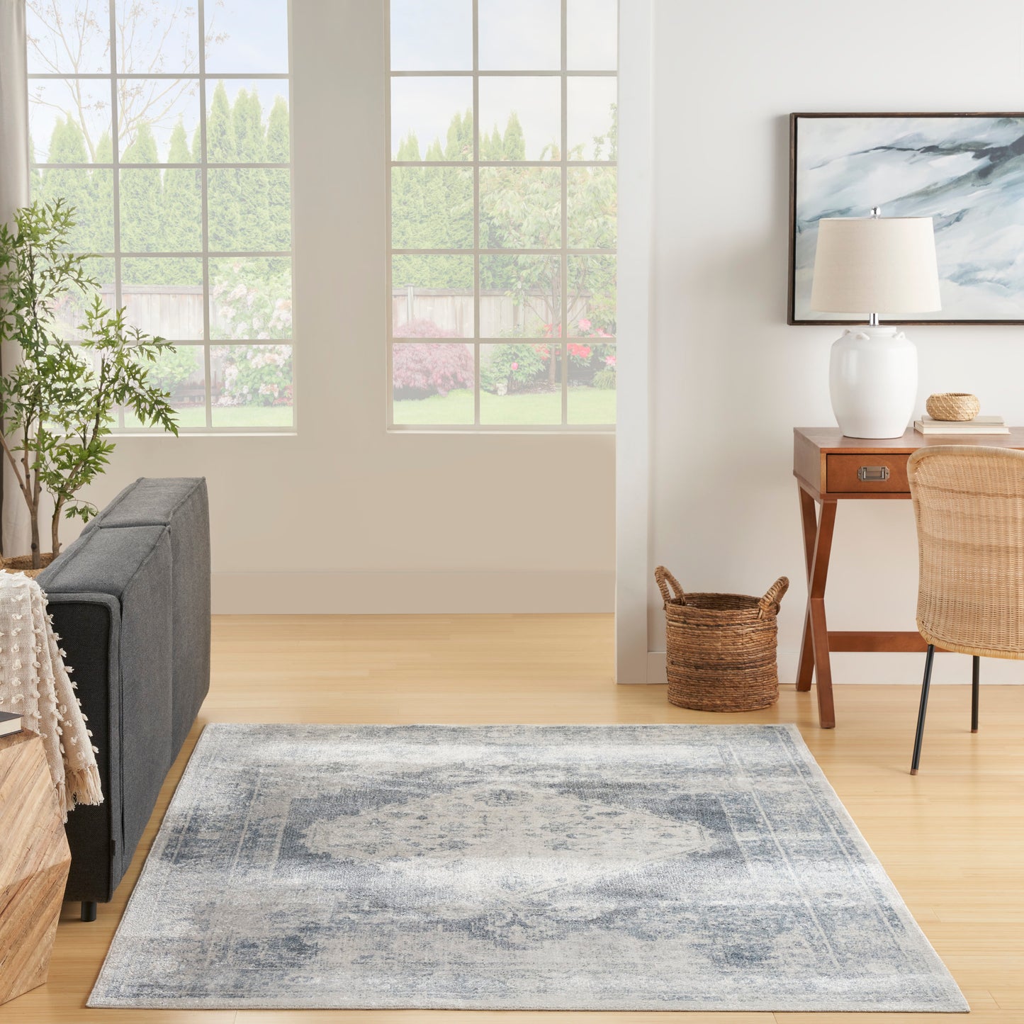 Rectangular blue-gray area rug on light wood floor in bright living room with gray sofa and wooden desk.
