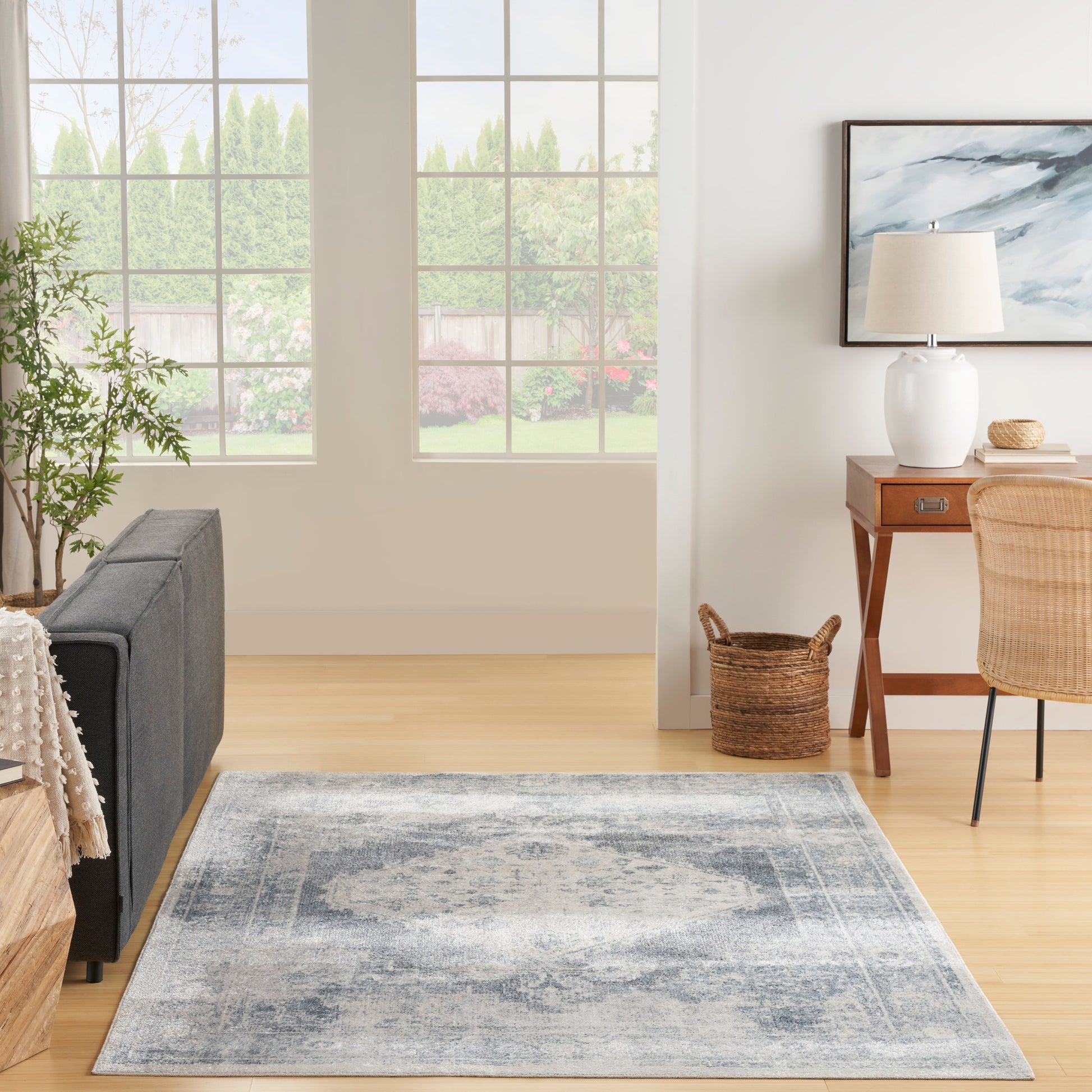 Rectangular blue-gray area rug on light wood floor in bright living room with gray sofa and wooden desk.