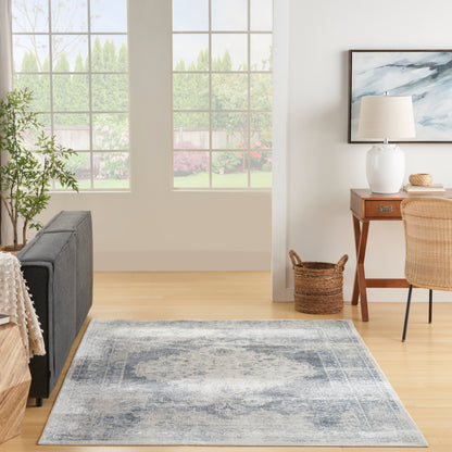 Rectangular blue-gray area rug on light wood floor in bright living room with gray sofa and wooden desk.