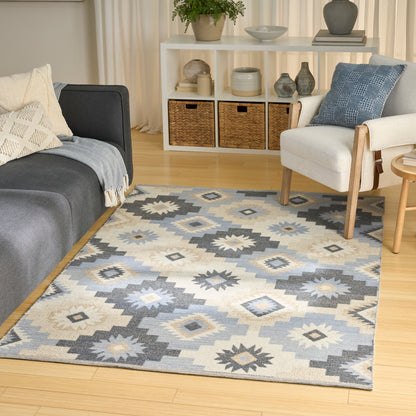 Diamond-pattern area rug in blue, gray and ivory tones in a modern living room with a gray sofa and cream armchair.
