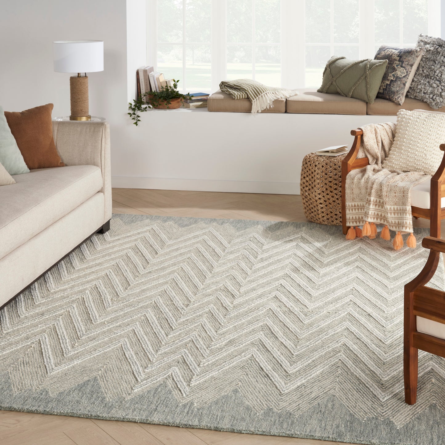 Soft grey chevron rug with cream zigzag pattern in a bright living room with beige sofa and wooden chairs.