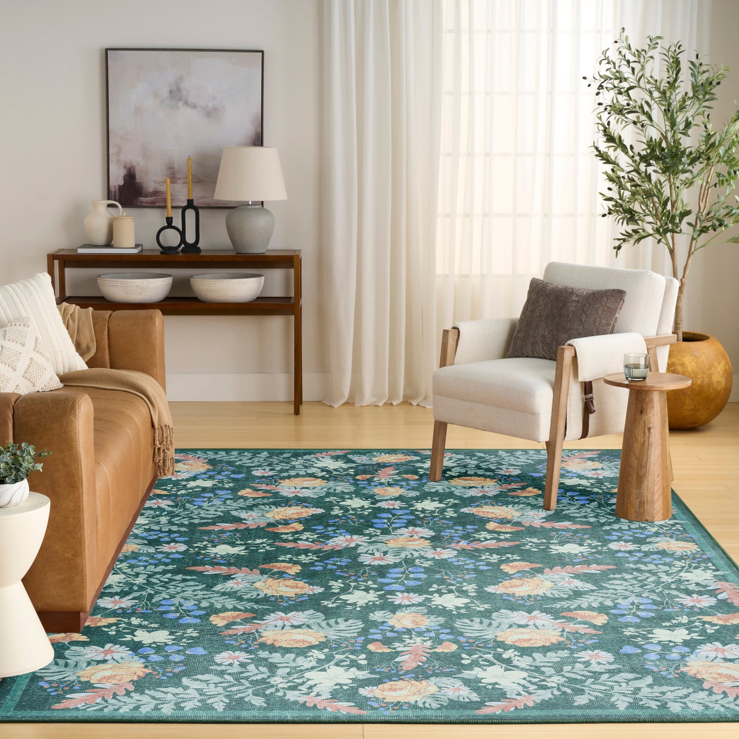 Cozy living room with teal floral area rug, tan leather sofa, white armchair, wooden console with bowls and candles, leafy plant.