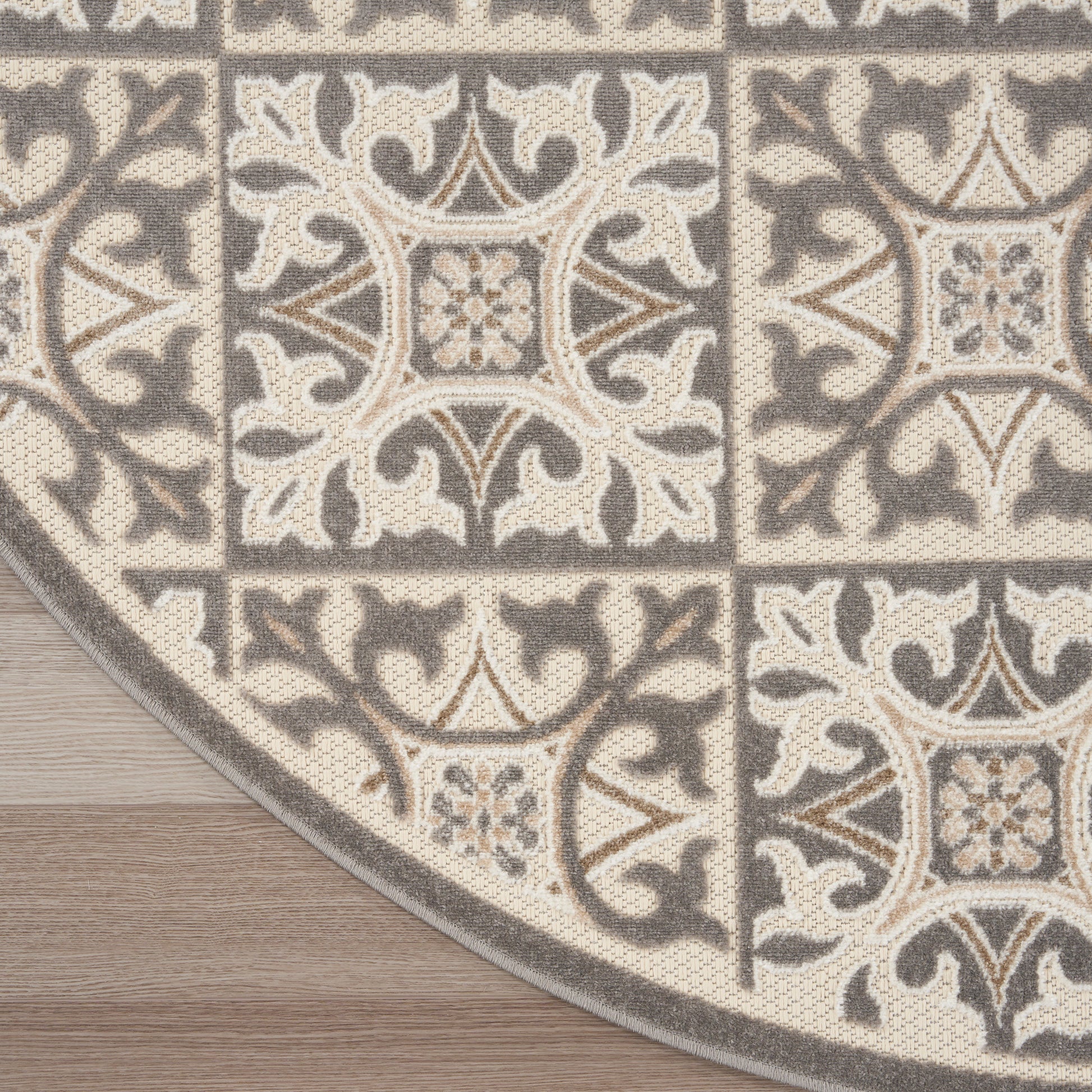Neutral-toned woven area rug with beige & gray ornate tile pattern, curved edge on wood floor.