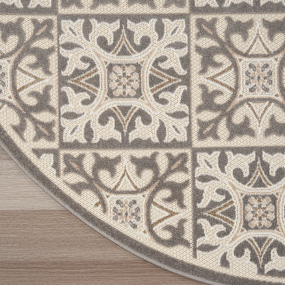 Neutral-toned woven area rug with beige & gray ornate tile pattern, curved edge on wood floor.