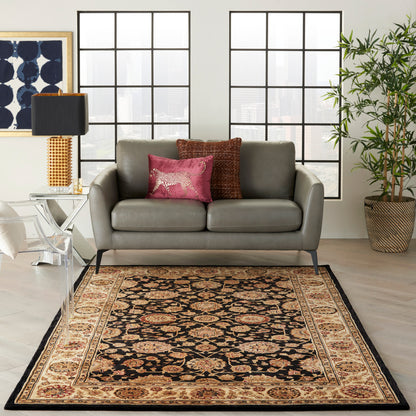 Gray leather sofa on a black-beige oriental rug; pink and copper cushions, acrylic chair, glass side table, tall lamp, potted plant.