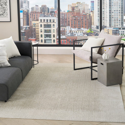 Modern living room with large city view, grey sofa, two black metal-framed chairs, beige rug, concrete side table with vase
