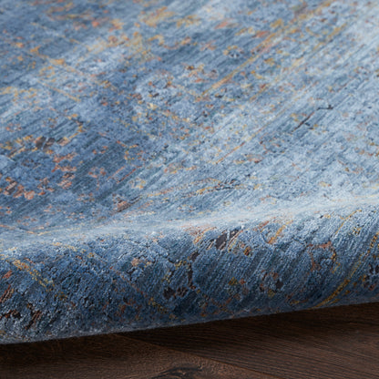 Blue textured rug with orange and tan distressed pattern on wood floor, edge curled.
