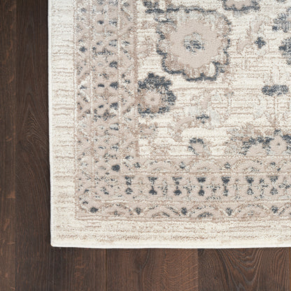 Rectangular cream and blue-gray oriental area rug with floral medallions and border on dark wood floor.