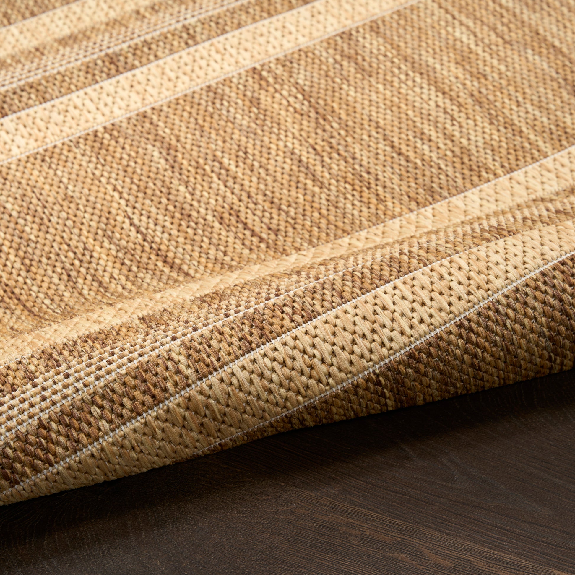Close-up of a natural fiber woven rug with beige and tan stripes and folded edge on dark wood floor.