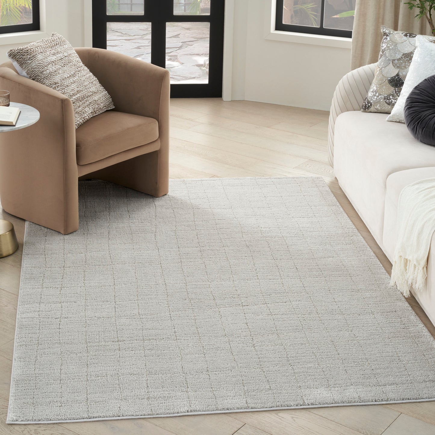 Light gray textured area rug with subtle grid pattern in a modern living room, tan armchair, white sofa, and natural light.