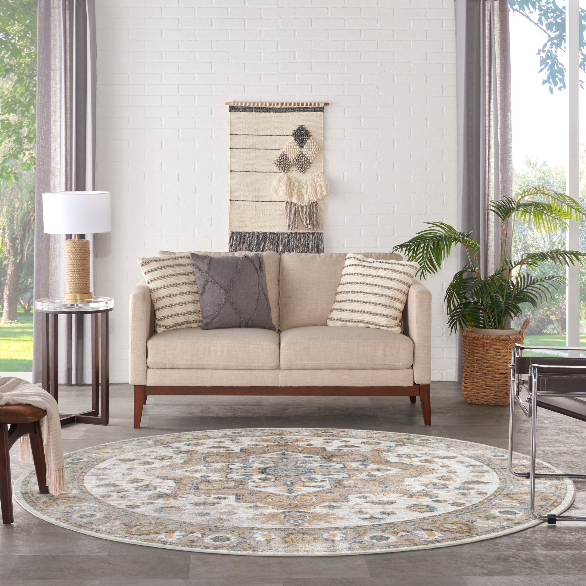 Beige mid-century sofa with wooden legs, gray/striped cushions, round patterned rug, woven wall hanging, lamp, and plant.