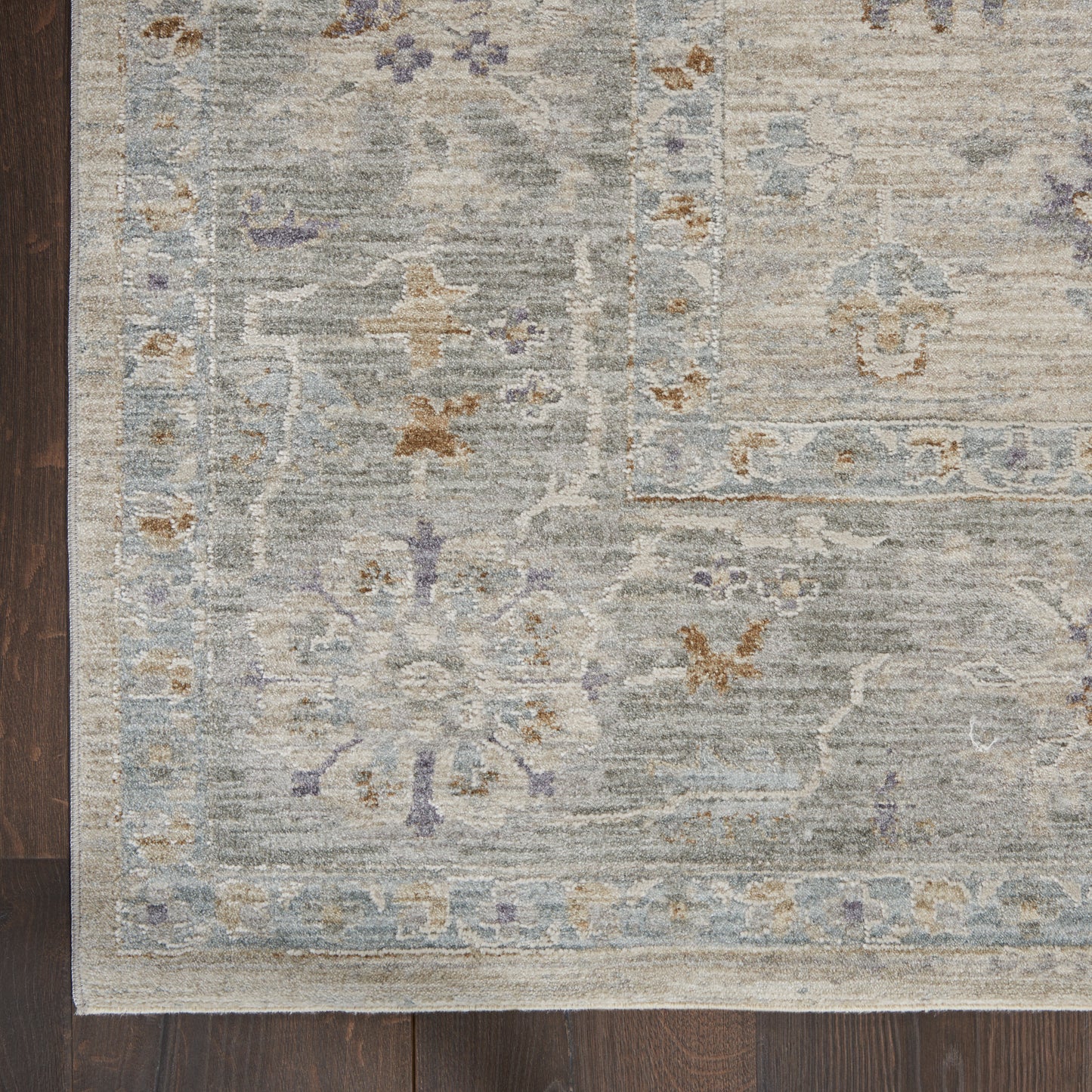 Distressed gray-blue oriental area rug with lavender floral motifs and pale border on dark wood floor.