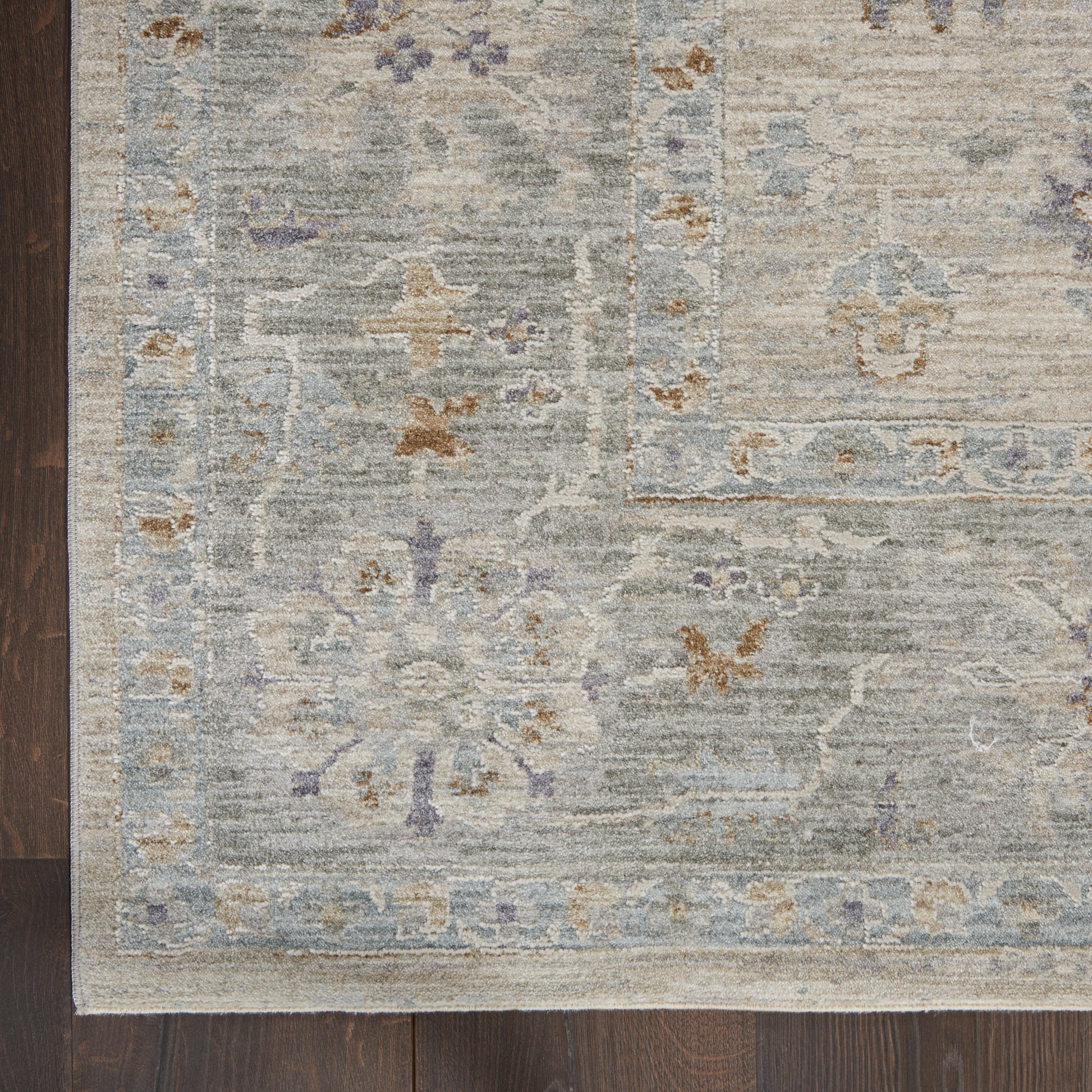 Distressed gray-blue oriental area rug with lavender floral motifs and pale border on dark wood floor.