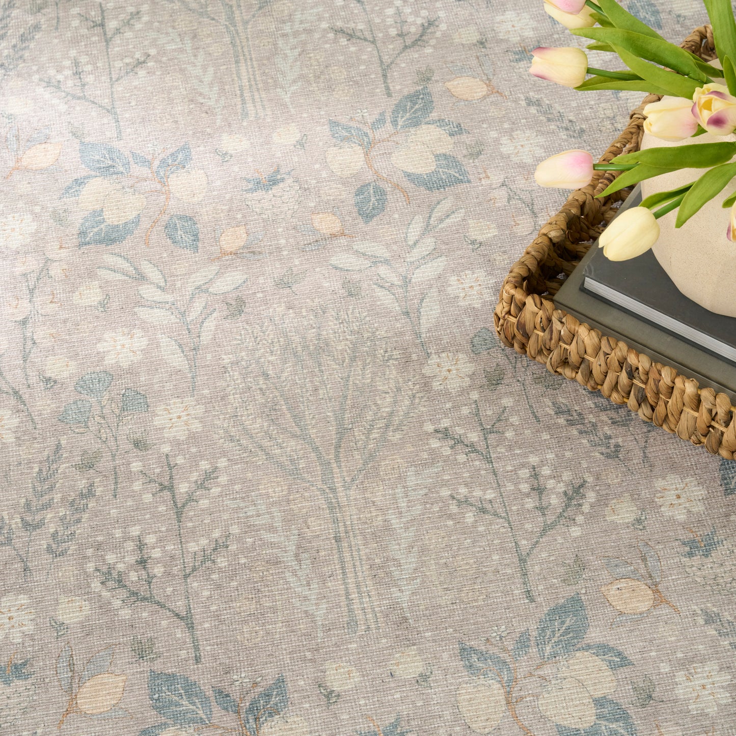Beige botanical area rug with light blue leaves; wicker tray with tulips atop books.