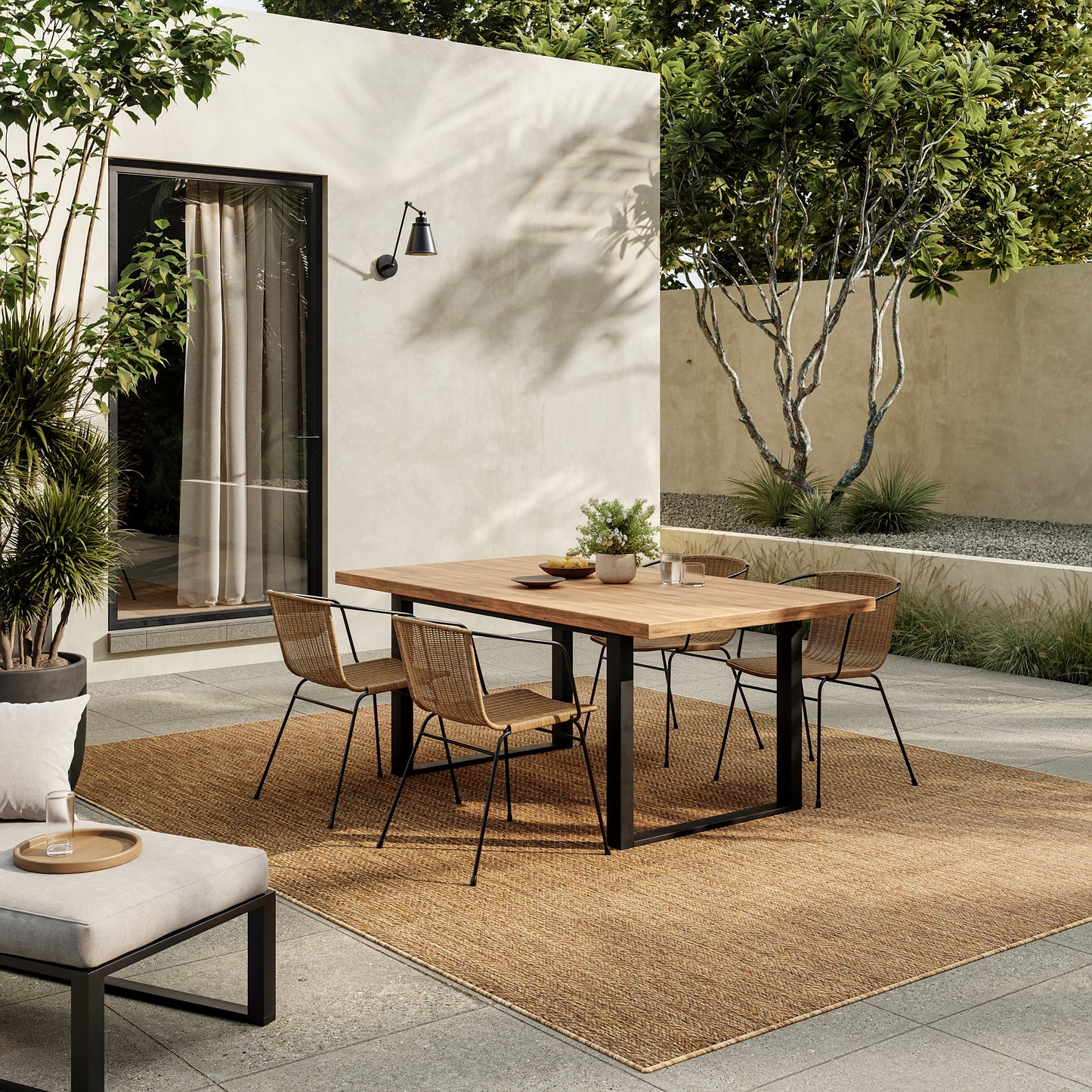 Outdoor dining set: wooden rectangular table with black legs, six rattan chairs on a natural fiber rug, beige stucco backdrop