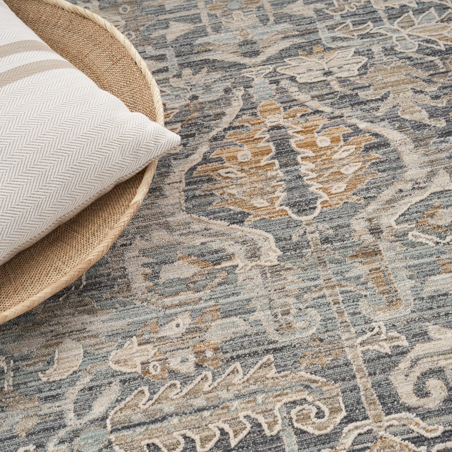Beige herringbone pillow in a round woven basket on a blue-gray and tan oriental rug.