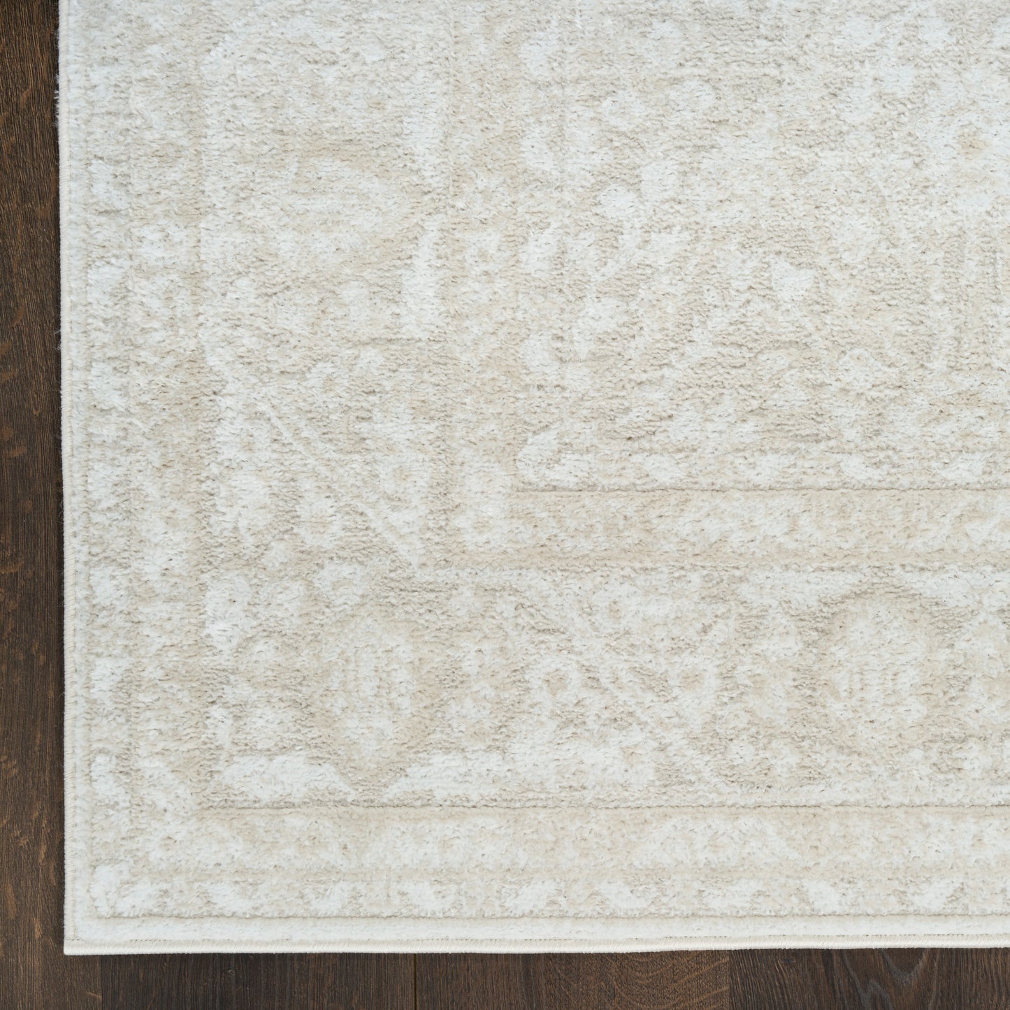 Rectangular beige patterned rug with subtle floral motifs and light border on dark wood floor.