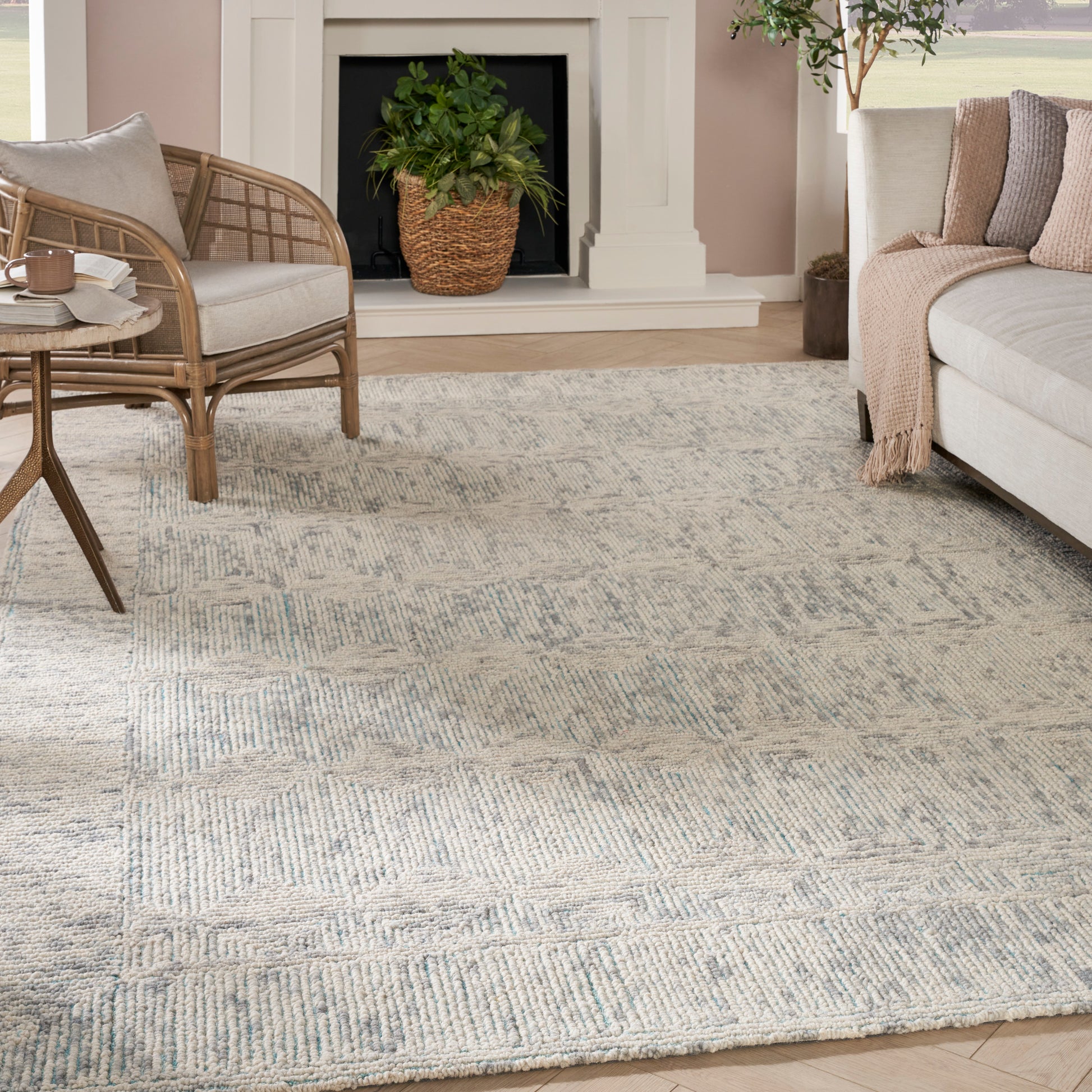Soft blue-gray geometric area rug anchors a cozy living room with a beige sofa, rattan chair, and fireplace.