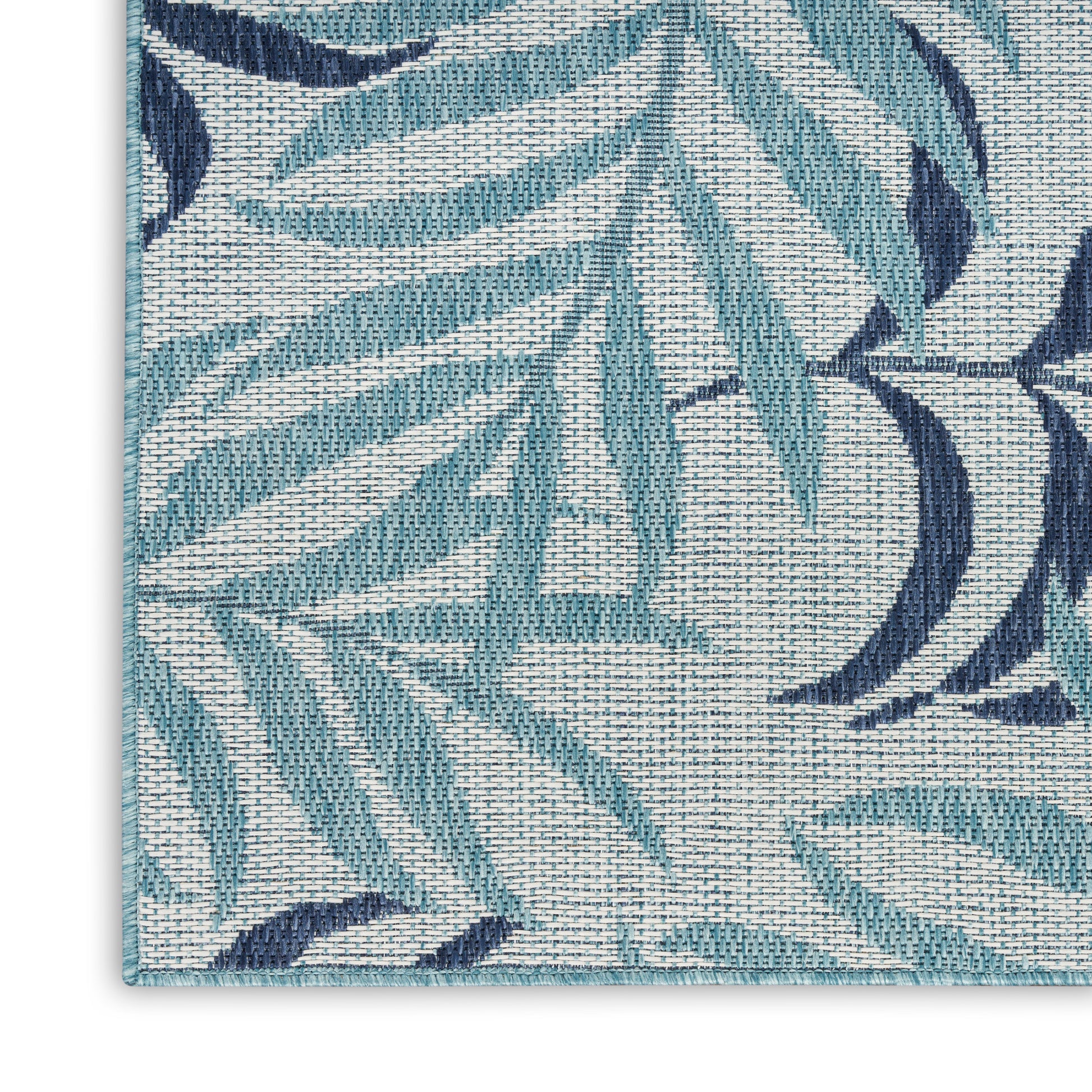 Close-up of teal and navy leaf-patterned woven rug with a textured cream background.