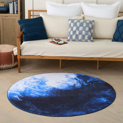 Circular blue ocean-wave rug on light wood floor beside a beige mid-century sofa with navy and light-blue pillows.