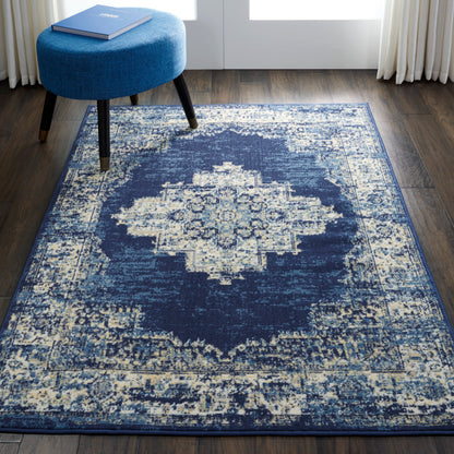 Navy blue area rug featuring a distressed ivory medallion center on dark wood floor, paired with a round blue ottoman.