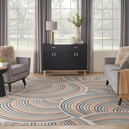 Living room scene with a black console cabinet, multicolor swirling rug, gray armchairs, plants, lamps & large windows.