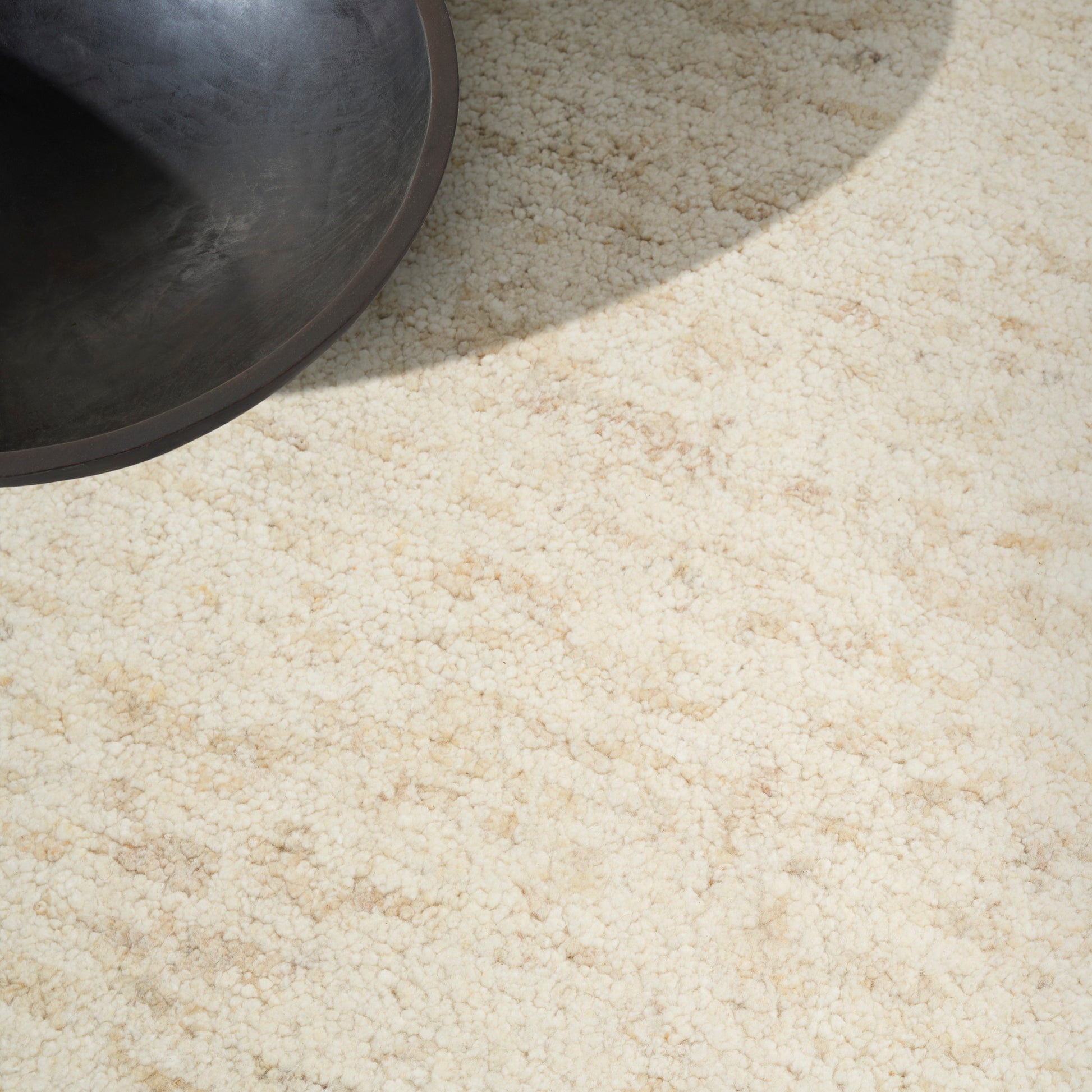 Partial view of a dark metal pot on a light beige textured carpet with a sunlight shadow