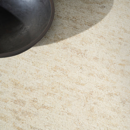 Partial view of a dark metal pot on a light beige textured carpet with a sunlight shadow