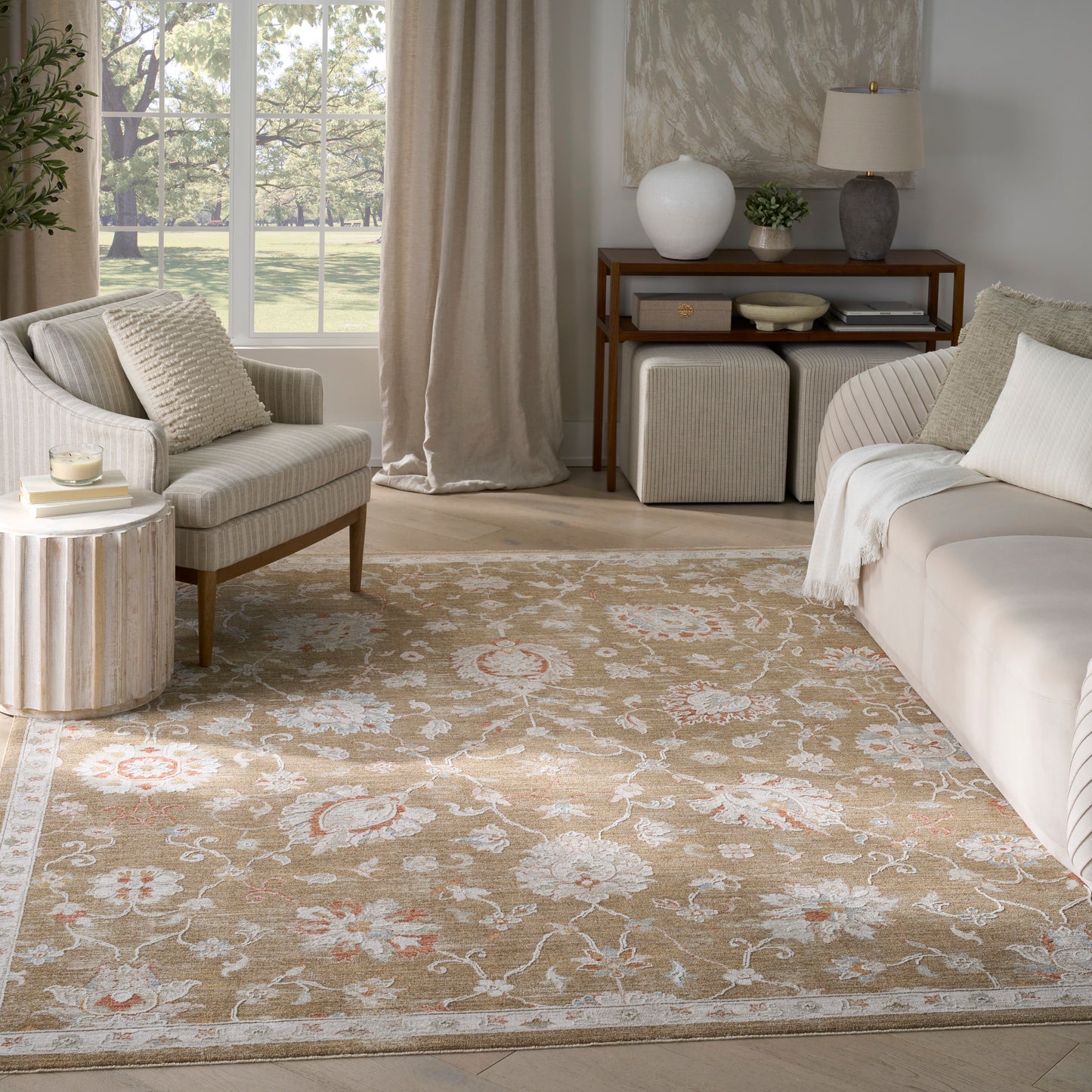 Neutral living room with beige floral area rug, cream sofa, striped armchair, wooden console, ottomans, plants.